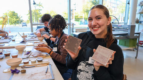 a student holds up two tiles they have decorated