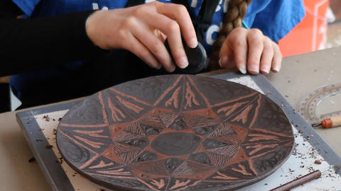 a person's hands burnishing a clay plate with a black on red carved design