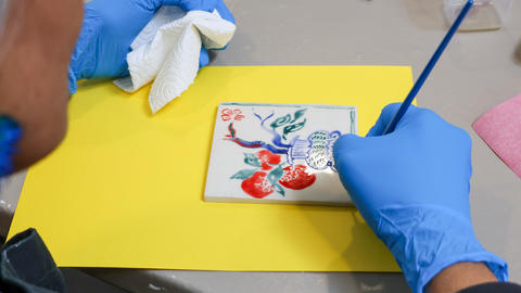 a person paints colors of china paint on a white tile