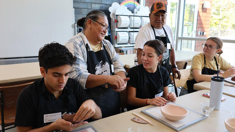 Wilma Baca Tosa assists a student making a pinch pot.