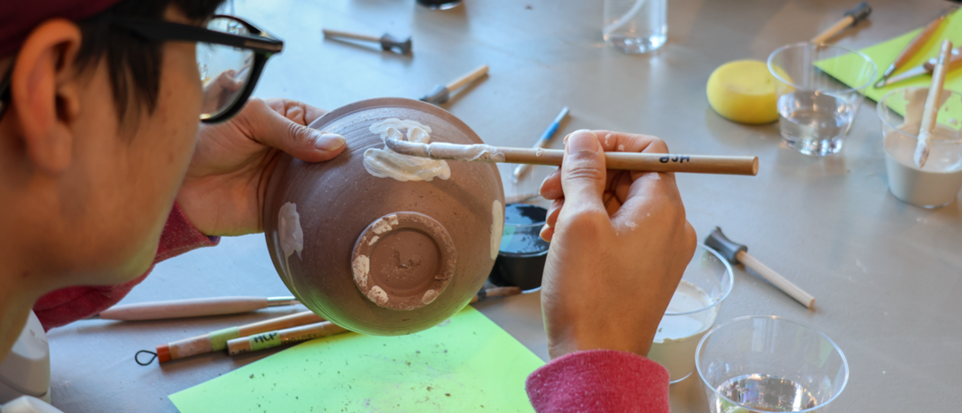 a student paints slip on a raw clay bowl