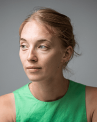 Close up of Ana Harmon. She has blond hair pulled back and looking off to the side. She's wearing a green tank top.