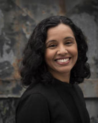 Black and white close-up headshot of Smitha Radhakrishnan smiling to the camera. She has chin-length hair.