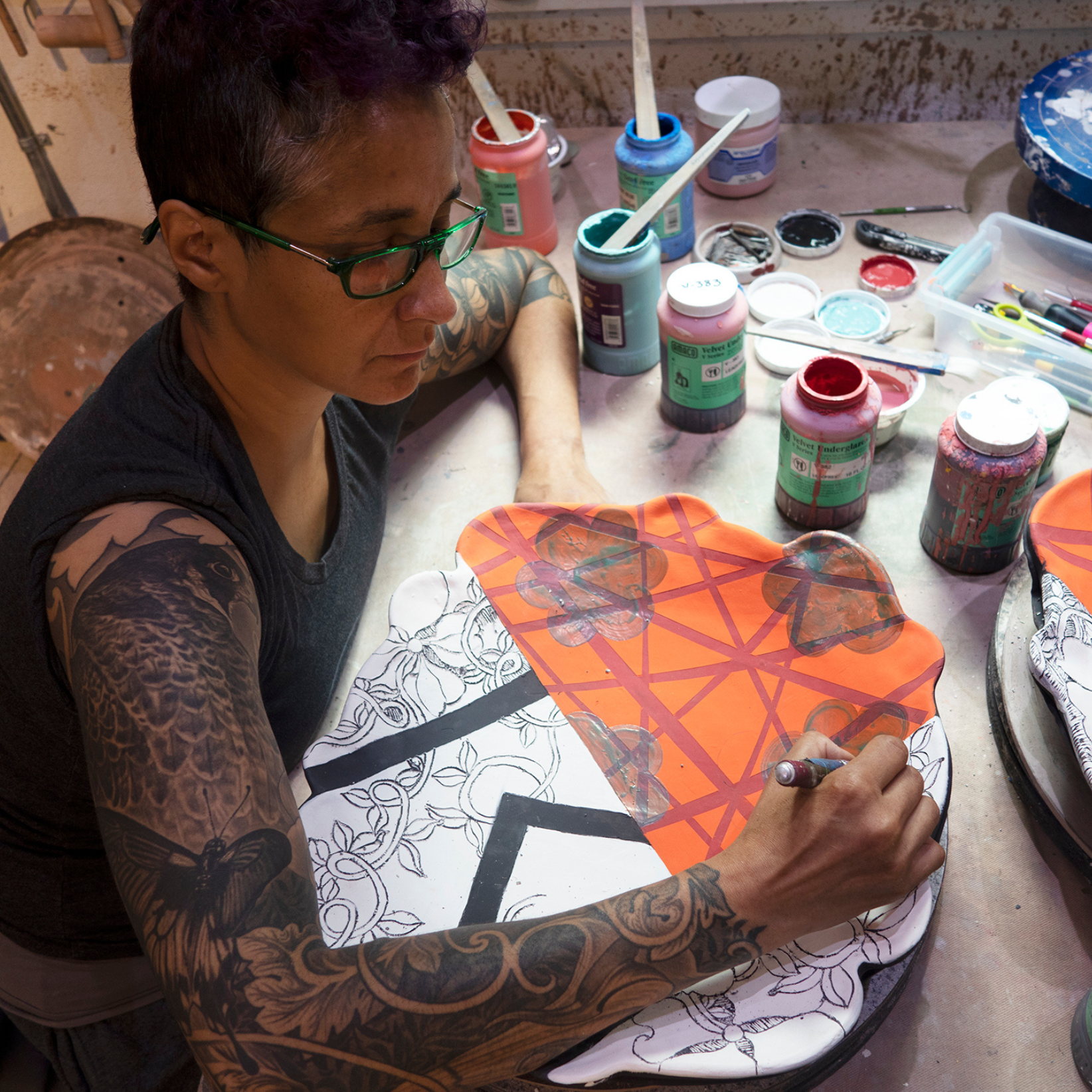 artist Adero Willard painting orange/red ceramic underglaze on a clay platter.