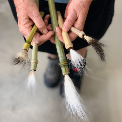 hands holding several handmade brushes made from bamboo