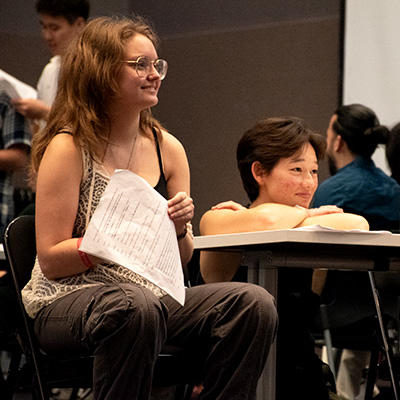 Students at a table, smiling while watching a rehearsal.