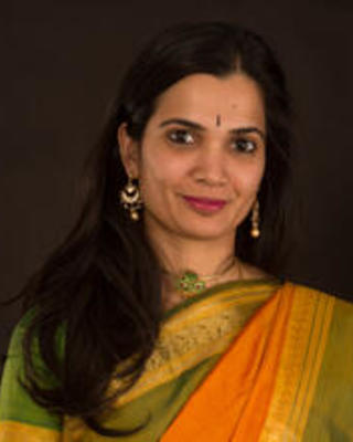 Headshot of Soumya Rajarim, an Indian woman with long brown hair, dangly earrings, and tear drop bindi. She is smiling subtly.