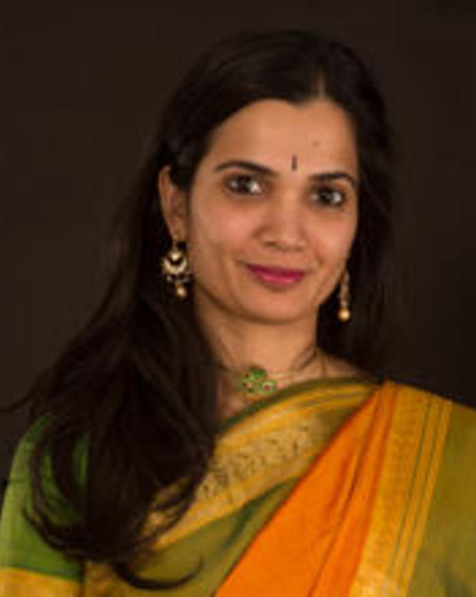 Headshot of Soumya Rajarim, an Indian woman with long brown hair, dangly earrings, and tear drop bindi. She is smiling subtly.